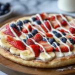 Sweet breakfast pizza with fresh strawberries, blueberries, bananas, and cream cheese frosting.